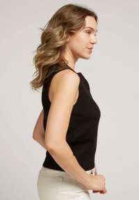 Top en maille sans manches noir avec un design ajusté, doté d'un col montant et d'une texture douce. Associé à un pantalon taillé de couleur claire.