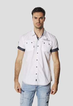 Cămașă albă cu mâneci scurte, accente bleu închis, două buzunare la piept și închidere cu nasturi. Prezintă cusături superioare și detaliu cu logo-ul brandului.