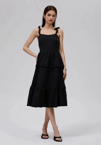 Μαύρο midi φόρεμα με εφαρμοστό μπούστο, δύο ιμάντες δέσιμο και πολυεπίπεδες πιέτες. Κατασκευασμένο από υφή υφάσματος, διαθέτει ανοιχτή σιλουέτα.