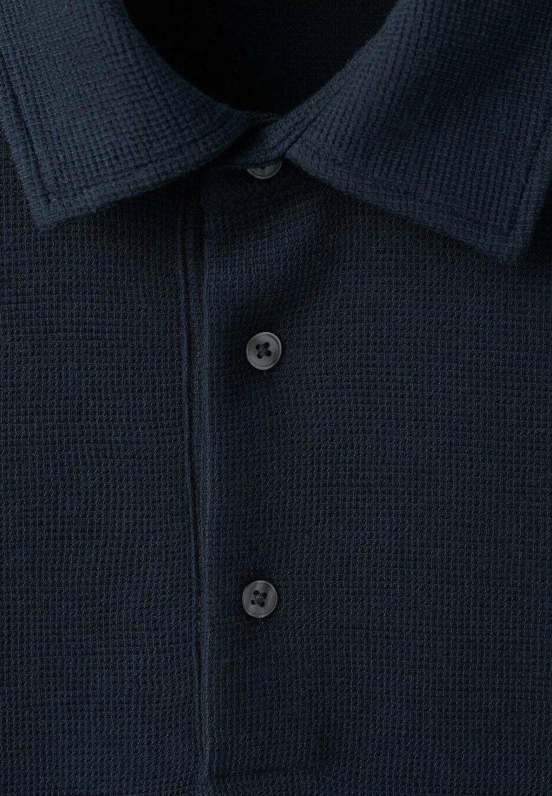 Polo bleu marine en tissu texturé avec un motif en grille, doté d'un col classique et de trois boutons noirs à l'avant.