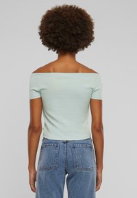 Lys grønn avskåret topp med korte ermer, tettsittende design og ribbet tekstur, parret med høyt liv blå denimjeans.