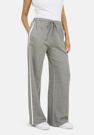 Grijze wijde sweatpants van zachte stof, met een witte zijstreep en een elastische tailleband met een trekkoord. Gepaard met witte sneakers.