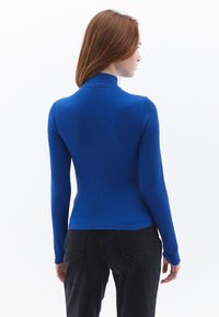 Langarm blauwe top in ribbeltextuur, met een hoge kraag en een fitted ontwerp. Gemaakt in combinatie met donkere broeken en een eenvoudige stijl.