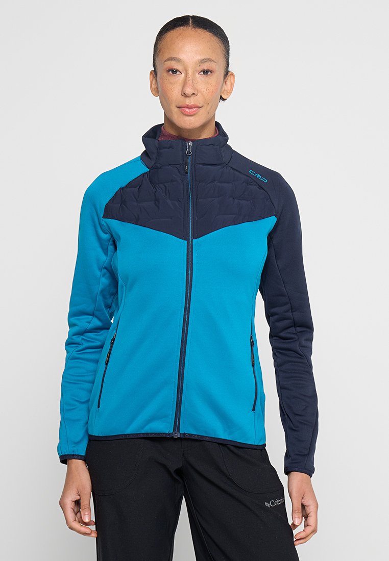 Blaue und marineblaue zip-up Jacke mit einem gesteppten oberen Bereich. Verfügt über einen weichen Stoff, hohen Kragen und zwei seitliche Taschen mit Reißverschlüssen.