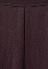 Temno rjavo blago s subtilnim teksturiranim vzorcem, ki ima osrednji šiv in pas na vrhu, kar ustvarja strukturiran videz.