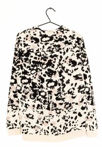 Gebreide trui met een witte achtergrond en een zwart-beige dierenprint. Lange mouwen, geribde manchetten en zoom. Hangt aan een zwarte haak.