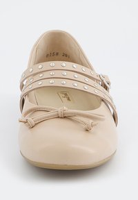 Beige kožené baleríny s dvěma ozdobnými pásky s stříbrnými nýty, detail s mašlí na špičce a kulatým siluetou.