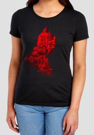 Frau trägt ein schwarzes T-Shirt mit rotem Batman-Profil-Grafik, gefüllt mit Zeitungsausschnitten und Gesichtern.