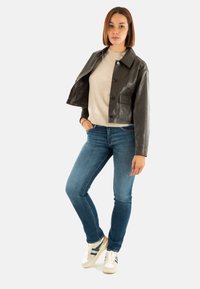 Giubbotto cropped in pelle nera, maglione beige sotto, jeans skinny blu e sneakers bianche con strisce blu navy. Materiali e texture contrastanti.