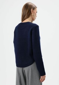 Pull en tricot bleu marine avec un col rond et des manches longues, doté d'un ourlet et de poignets côtelés, vu de dos.