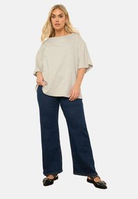 Blusa de corte suelto en gris claro con mangas amplias, combinada con jeans acampanados de color azul oscuro. Zapatos planos negros con acentos decorativos.