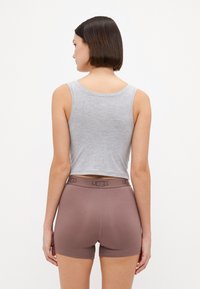 Débardeur gris court et short en boxer marron avec un logo UGG sur la ceinture. Texture douce avec un design ajusté.