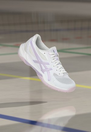 Scarpa sportiva bianca e viola chiaro con materiali a rete e sintetici, che fluttua sopra un pavimento di palestra interna con linee colorate del campo.
