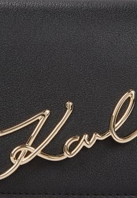 Black textured leather with gold signature accent, featuring a smooth metallic finish. Compact design suitable for accessories or wallets.