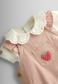 Robe bébé en velours côtelé rose avec poche avant ornée d’un patch fraise texturé et une chemise blanche avec col en dentelle ajourée et imprimé fraises.