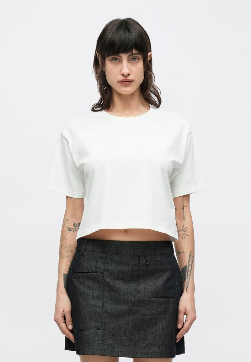 Przycięty biały bawełniany t-shirt z okrągłym dekoltem i krótkimi rękawami, połączony z ciemnoszarą spódnicą jeansową z dwoma przednimi kieszeniami.