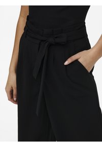 Svarta högmidjade byxor med en knuten rosett-bälte, veck och sidofickor. Slät tyg, skräddarsydd passform och inga synliga mönster.