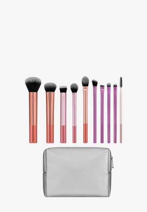 Dziesięć różnych pędzli do makijażu z uchwytami w kolorze różowego złota i fioletu, ułożonych nad srebrną kosmetyczką na zamek.