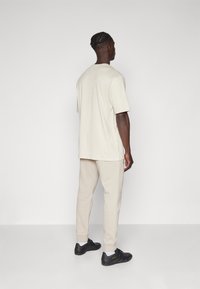 Beige Baumwoll-T-Shirt mit kurzen Ärmeln und passende Jogginghose mit gerippten Bündchen, kombiniert mit schwarzen Sportschuhen. Schlichte Gestaltung, keine sichtbaren Muster.