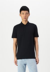 Polo preto em algodão com mangas curtas, colarinho plano e abertura de três botões. Usado com jeans azul claro.