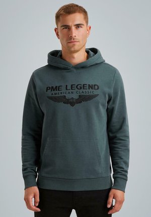 Groene hoodie van zacht materiaal, met een voorzak, een capuchon met trekkoord en zwarte teksten met een gevleugeld logo op de borst.