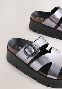 Metalické strieborné sandále na platforme s korkovou stielkou, čiernou podrážkou, dizajnom s výrezmi a nastaviteľným detailom na pracku.