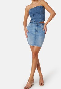 Top crop in denim e minigonna aderente in azzurro chiaro, con scollo dritto e passanti per cintura. Modella che indossa sandali trasparenti con tacco.