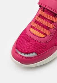 Rosa Sneaker mit einer Mesh-Oberfläche, reflektierenden Akzenten, strukturiertem Stoff und lila-orange gestreiften Schnürsenkeln. Weiße Sohle.