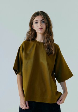 Oliven grøn, oversized top med korte ærmer og rund halsudskæring, lavet af et glat materiale. Centreret på en model mod en neutral baggrund.