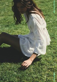 Žena v bielych dlhých rukávoch sediaca na tráve, jemne sa dotýkajúca zeme, s textom „Nová kolekcia“ v pravom hornom rohu.