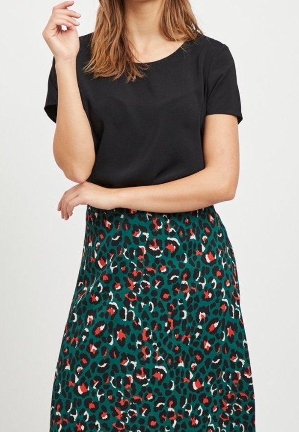 Haut noir à manches courtes associé à une jupe verte à imprimé léopard avec des accents rouges et blancs, en tissu lisse et coupe décontractée.