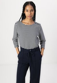 Camisa de manga larga a rayas con rayas horizontales negras y blancas, combinada con pantalones de talle alto en color marino con cinturón.