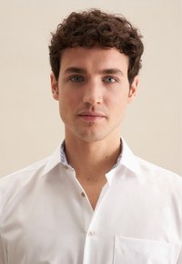 Camicia bianca con un taglio su misura, caratterizzata da un colletto interno a fantasia blu e una tasca sul petto, realizzata in tessuto morbido.