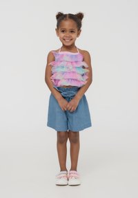 Top a maniche corte colorato con ruches nei toni del rosa, blu e lavanda; pantaloncini di jeans con vita a lacci; scarpe con velcro rosa e blu.