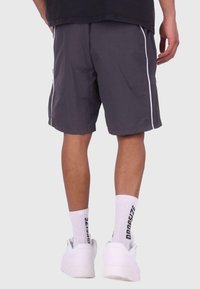 Grå shorts med hvide sidelister, lavet af letvægtsmateriale. Båret med hvide sneakers og mønstrede ankelsokker.