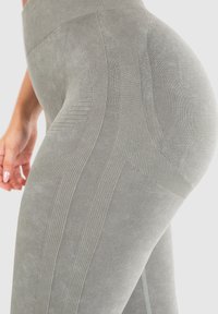 Lekko szare legginsy z wysokim stanem, wykonane z teksturowanej tkaniny, z akcentami w prążki i pionowymi liniami, nadającymi sylwetce smukły wygląd.