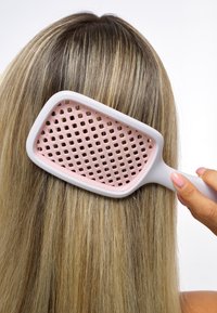 Rektangulär hårborste med vitt handtag och rosa perforerad botten, som reder ut rakt, blont hår från hårbotten.