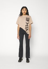 Beige, túlméretezett póló fekete "NIKE" logóval átlósan az elején, fekete csípőfazonú nadrággal és fekete platform cipőkkel párosítva.