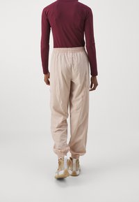 Lichtroze sportbroek met elastische tailleband en boorden, gecombineerd met beige sneakers met opvallende accenten en een gestructureerd ontwerp.