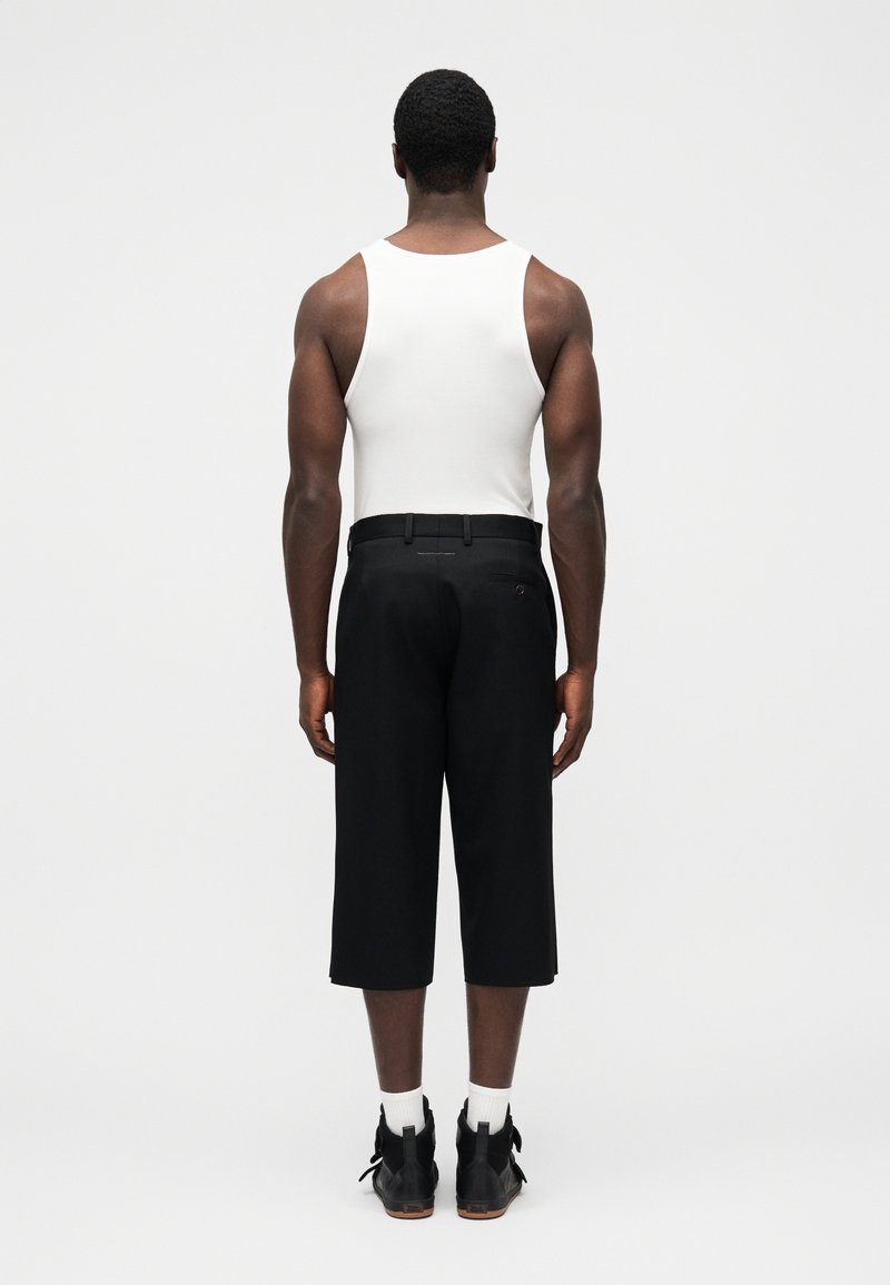 Pantalon noir court associé à un débardeur blanc, présentant une texture lisse et une poche arrière avec un détail de logo subtil.