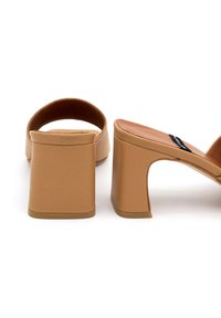 Mule con tacco a blocco color tabacco, apertura sul retro, in pelle liscia, punta squadrata e tacco basso e largo per una maggiore stabilità. Design semplice.