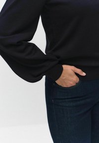 Svart tröja med voluminösa ärmar, ribbade mudd och en slät textur. Matchad med mörkblå jeans med en klassisk fickdesign.