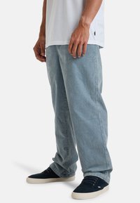 Jeans en denim délavé bleu clair avec une coupe décontractée et des jambes droites, associés à des baskets sombres avec une touche en toile.