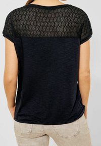 Černé tričko s texturovanou, průhlednou horní částí s cik-cak vzorem. Měkká tkanina, volný střih, krátké rukávy a zaoblený lem.