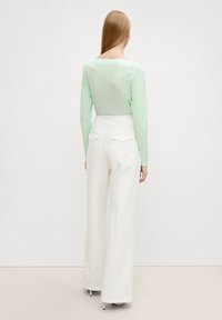 Miętowozielona bluzka z długim rękawem i wycięciem na plecach, połączona z białymi spodniami z wysokim stanem i szerokimi nogawkami, posiadającymi dwie tylne kieszenie.