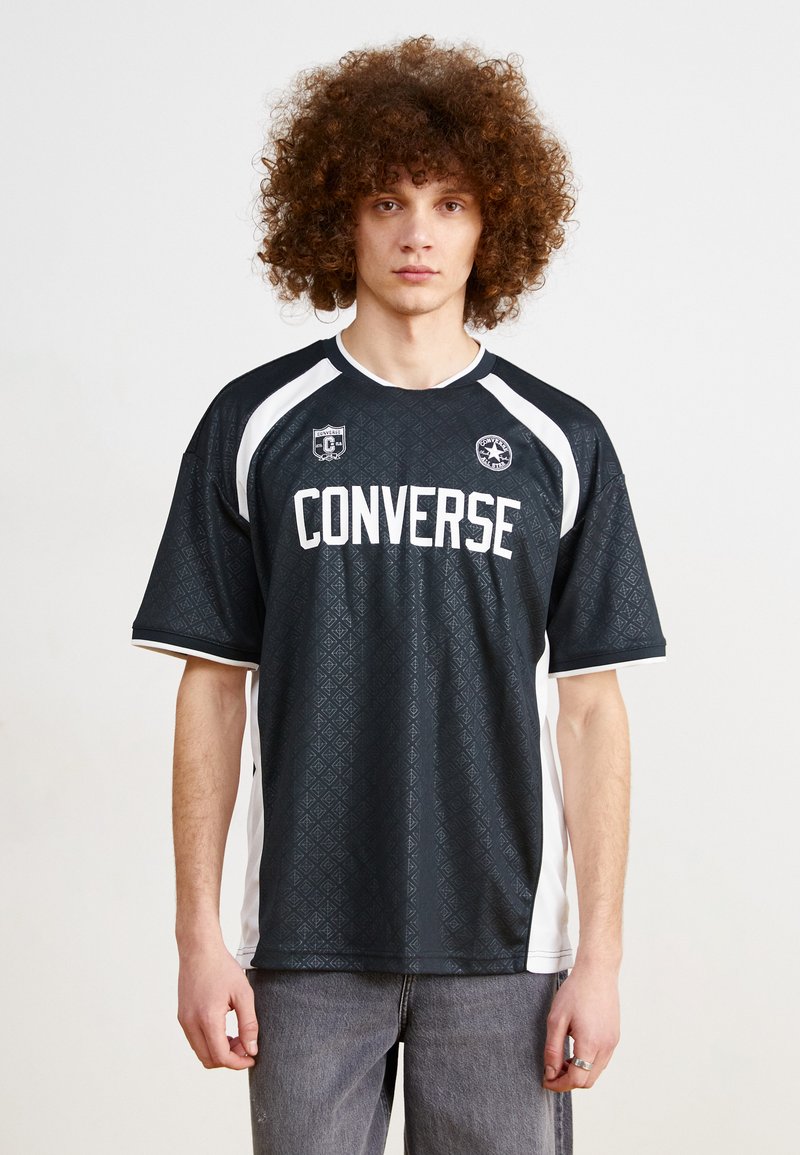 Camiseta corta de manga negra con un patrón de diamantes texturizado, detalles en blanco y el logotipo "CONVERSE" en letras grandes en la parte frontal.