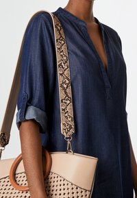 Jeansowa bluzka z plisą i podwiniętymi rękawami, w parze z beżową torebką o tkanej fakturze i paskiem w wężowy wzór.