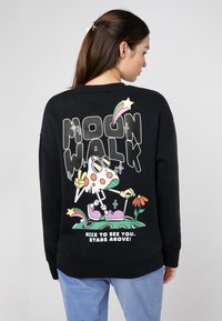 Schwarzer Sweatshirt mit einem bunten Grafikdruck auf der Rückseite, der eine Cartoonfigur mit einem Peace-Zeichen, Blumen und Text darstellt.
