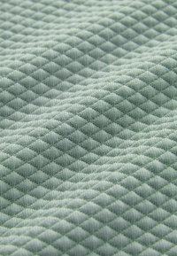 Tejido verde claro texturizado con un patrón de diamantes, que presenta una apariencia suave y acolchada que resalta la profundidad y los detalles del tejido.