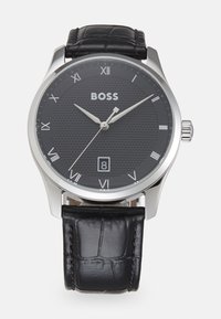 Reloj con correa de cuero negro, esfera negra texturizada, manecillas en tono plateado, números romanos y display de fecha a las 6 en punto; caja de acero inoxidable.